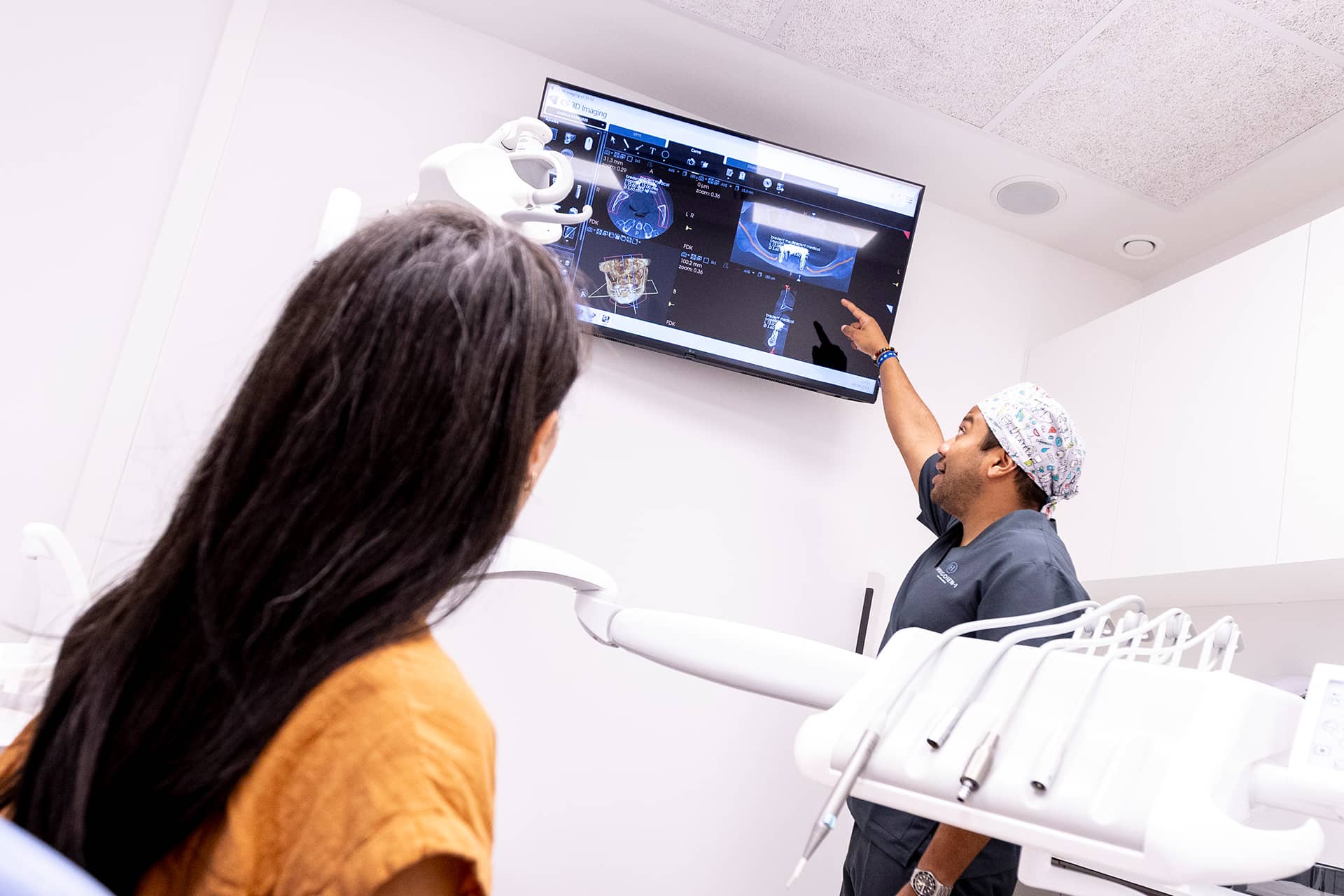 Profesionalak inplante bat jartzeko tratamendu bat azaltzen dio paziente bati pantaila baten aurrean.